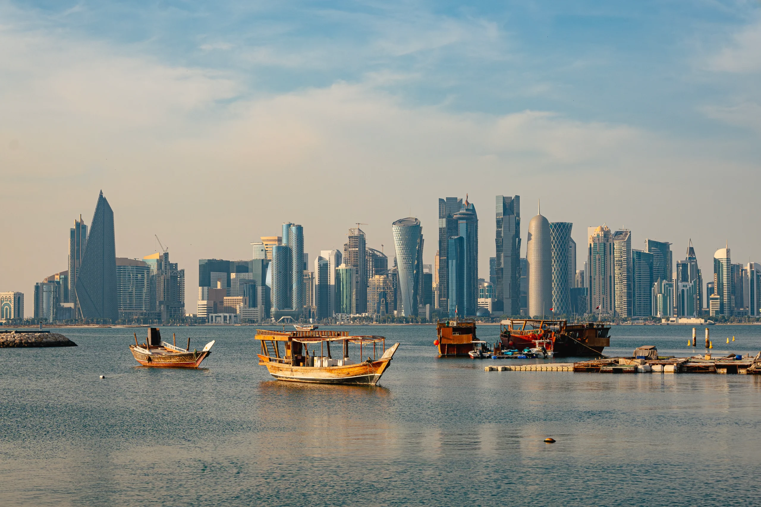 Traditional wooden Qatari dhow sailing on Doha Bay with the illuminated West Bay skyline at sunset